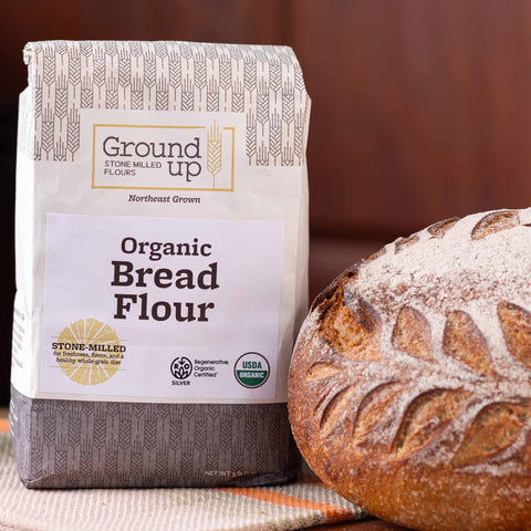 A 3 pound bag of Ground Up Organic Bread Flour, with a loaf of sourdough bread